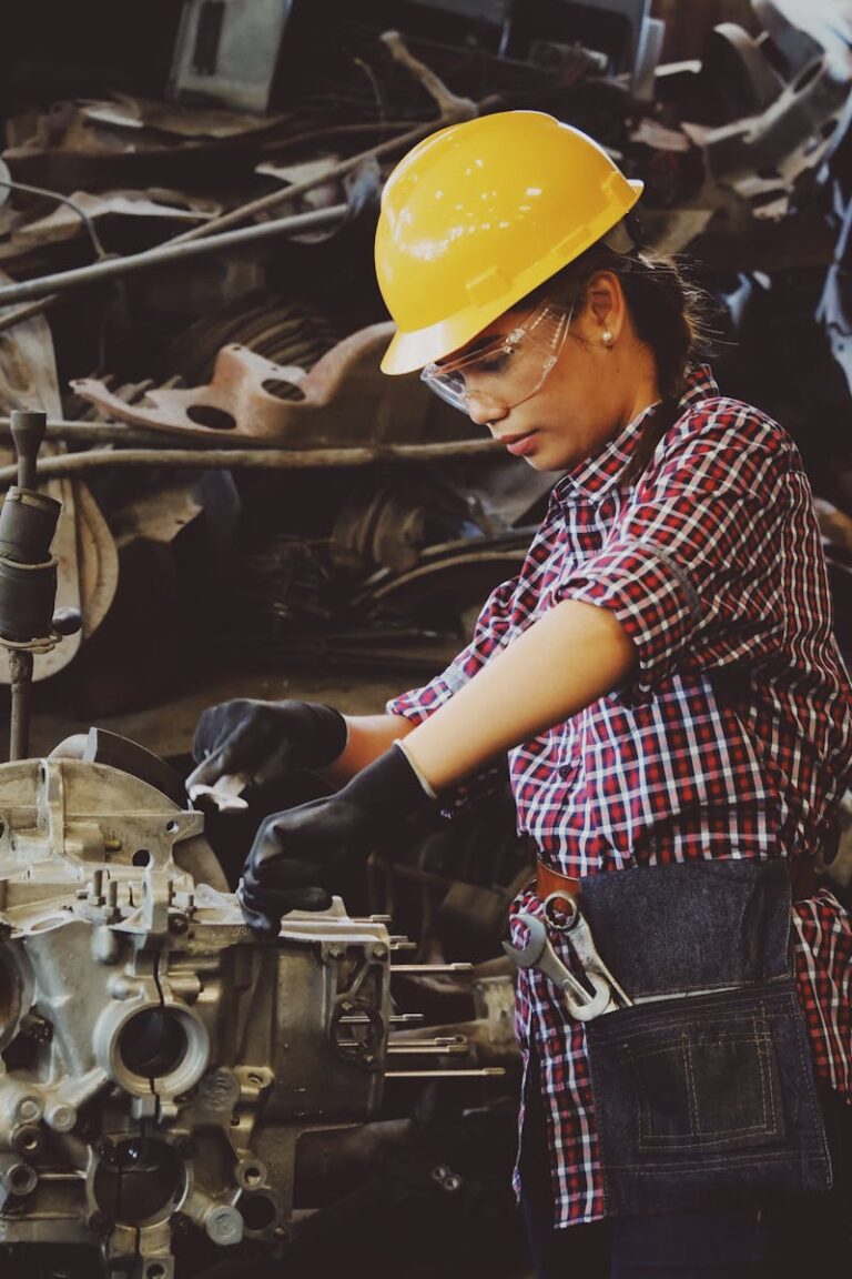 Woman engineer wearing safety gear, working on machine repair in an industrial setting.